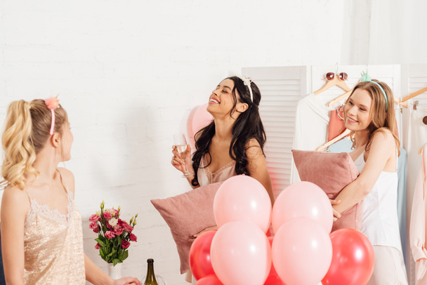 schöne fröhliche multiethnische Mädchen in Nachtwäsche feiern mit Gläsern Champagner und Luftballons während Pyjama-Party - Foto, Bild
