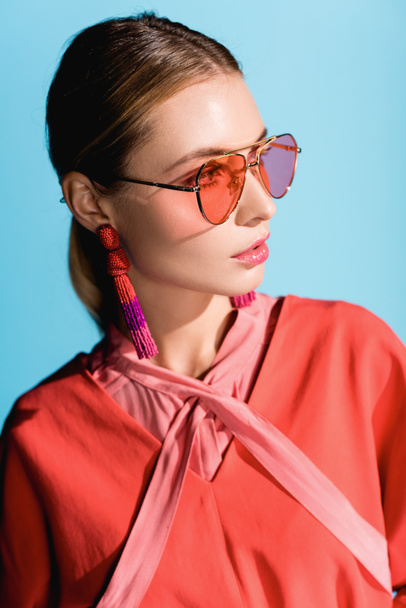 attractive stylish woman in trendy living coral clothing and sunglasses posing isolated on blue - Zdjęcie, obraz