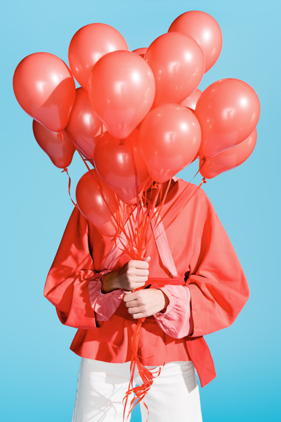 stylish girl posing with living coral balloons in front of the face isolated on blue - Zdjęcie, obraz