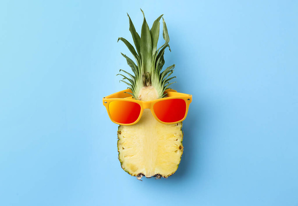 Funny pineapple with orange sunglasses on blue background, top view - Zdjęcie, obraz