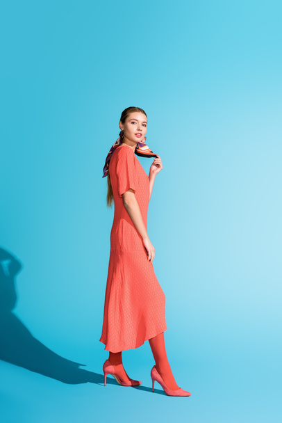 модная элегантная модель в модном живом коралловом платье, позирующем на голубом
 - Фото, изображение