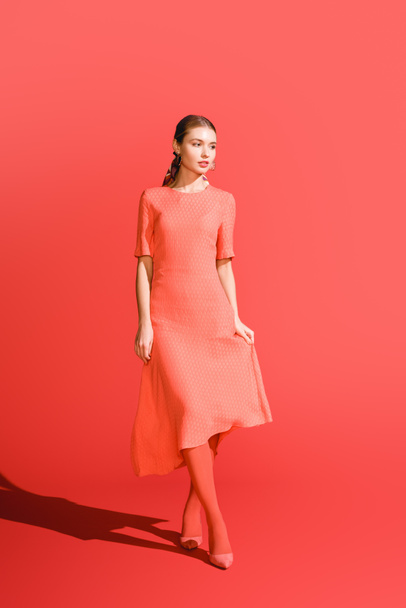 stylish girl posing in living coral dress on red background - Zdjęcie, obraz