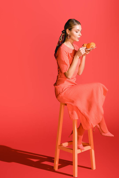 fashionable woman holding plate with macaroons on living coral. Pantone color of the year 2019 concept - Photo, Image