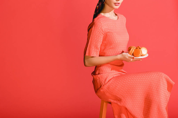 vista ritagliata di elegante ragazza in possesso di piatto con macaron isolati su corallo vivente. Pantone colore dell'anno 2019 concept
 - Foto, immagini