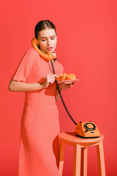 piękna kobieta z makaroniki i vintage obrotowy telefonu na białym tle na życia koralowców. PANTONE kolor koncepcja rok 2019 - Zdjęcie, obraz
