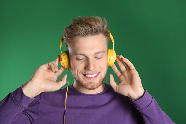 Handsome young man listening to music with headphones on color background - Foto, imagen
