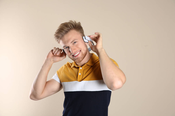 Handsome young man listening to music with headphones on color background - Фото, изображение