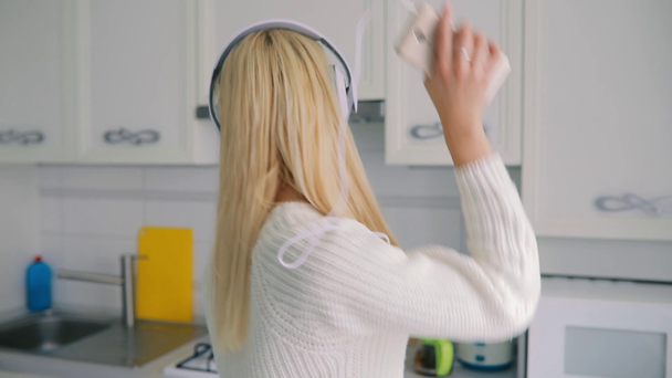 Ξέγνοιαστες νεαρή γυναίκα που χορεύει στην κουζίνα ακούγοντας μουσική - Πλάνα, βίντεο