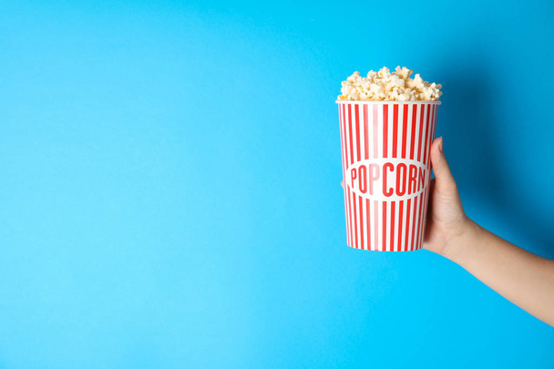 Woman holding popcorn cup on color background, closeup with space for text. Cinema snack - Фото, изображение