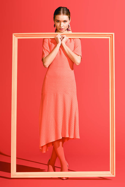 fashionable elegant girl in dress posing with big frame on living coral. Pantone color of the year 2019 concept - Фото, зображення