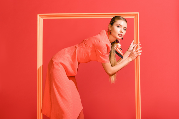 attractive girl in dress posing with big frame isolated on living coral. Pantone color of the year 2019 concept - Foto, afbeelding