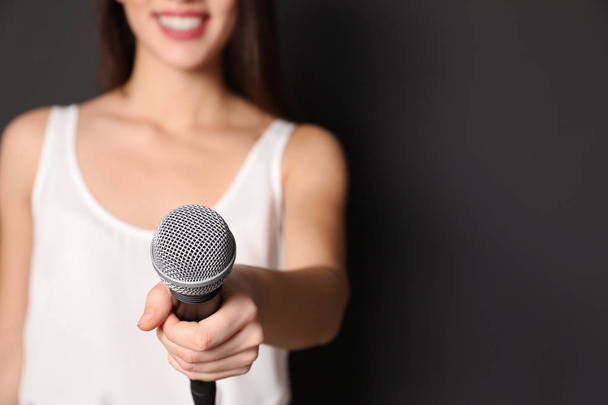 Young woman holding microphone on dark background, closeup view with space for text - Foto, Imagen