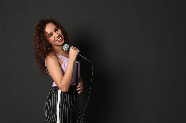 Curly African-American woman singing in microphone on color background - Valokuva, kuva