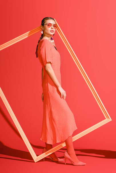 fashion shoot with elegant girl in dress posing with big frame on living coral. Pantone color of the year 2019 concept - Foto, immagini