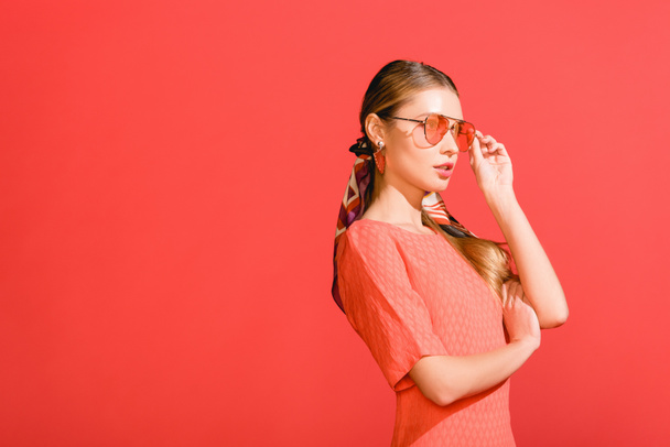 divatos lány pózol élő korall ruha és piros háttér elszigetelt napszemüveg - Fotó, kép