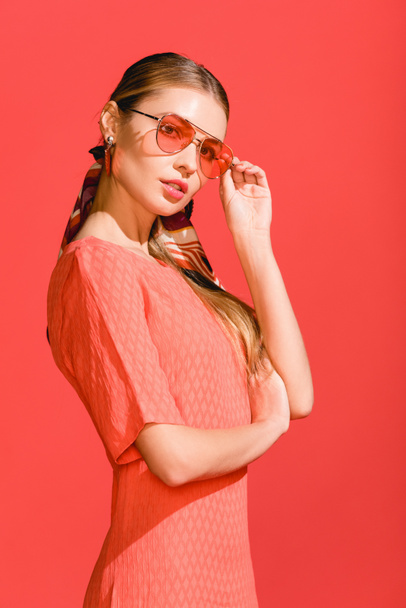 fashionable model posing in living coral dress and sunglasses on red background - Фото, изображение