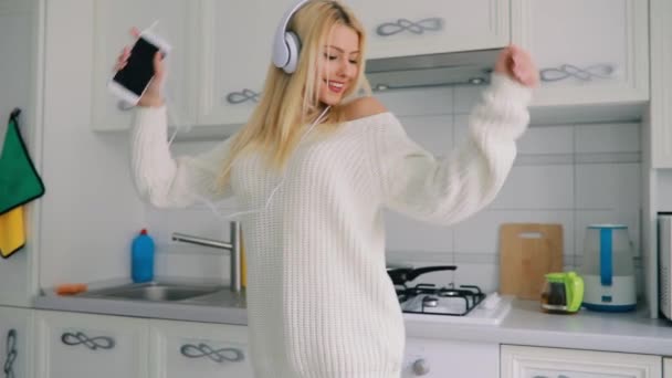 Carefree young woman dancing in kitchen listening to music - Materiał filmowy, wideo
