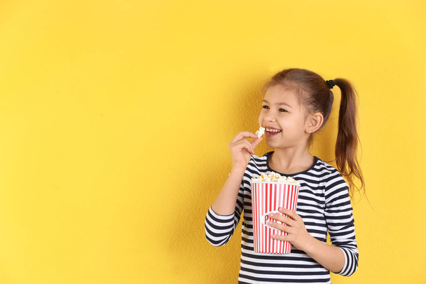 Cute little girl with popcorn on color background. Space for text - Photo, image