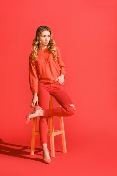 stylish elegant girl posing in living coral clothing on stool on red background - Photo, image