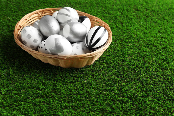 Wicker basket of painted Easter eggs on green lawn, space for text - Foto, Imagem