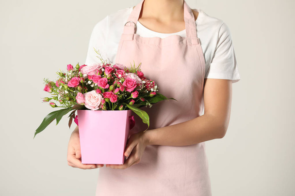 Woman holding paper gift box with flower bouquet on light background, closeup - Φωτογραφία, εικόνα