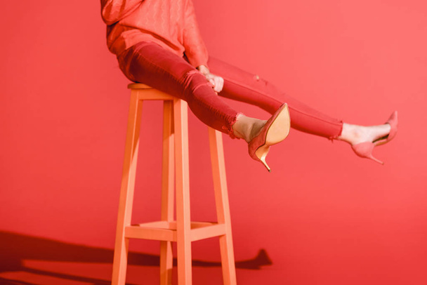 cropped view of fashionable girl posing in living coral clothing on stool on red background - Photo, Image