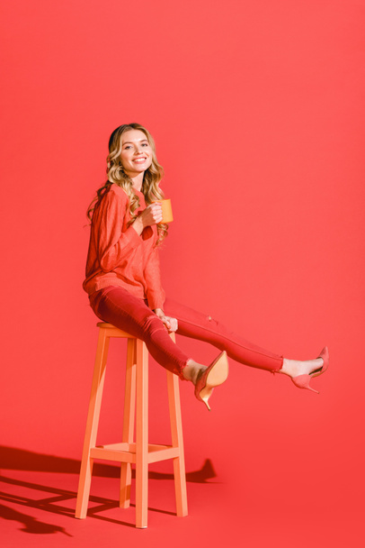 happy stylish girl with cup of coffee sitting on stool on living coral. Pantone color of the year 2019 concept  - Foto, immagini