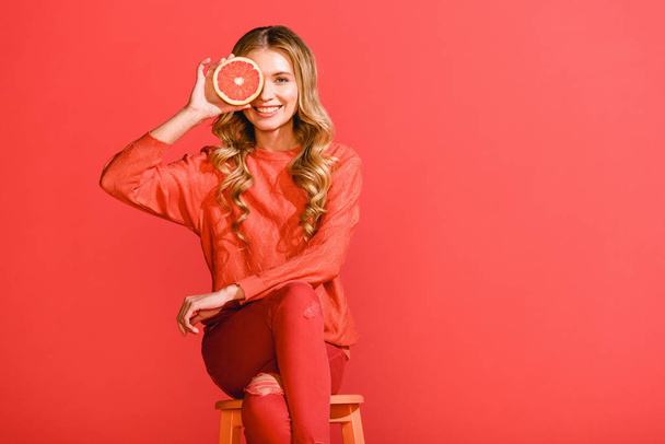 smiling fashionable girl posing and grapefruit isolated on living coral. Pantone color of the year 2019 concept - Фото, изображение