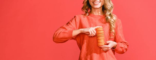cropped view of woman holding sweet macaroons isolated on living coral. Pantone color of the year 2019 concept - 写真・画像