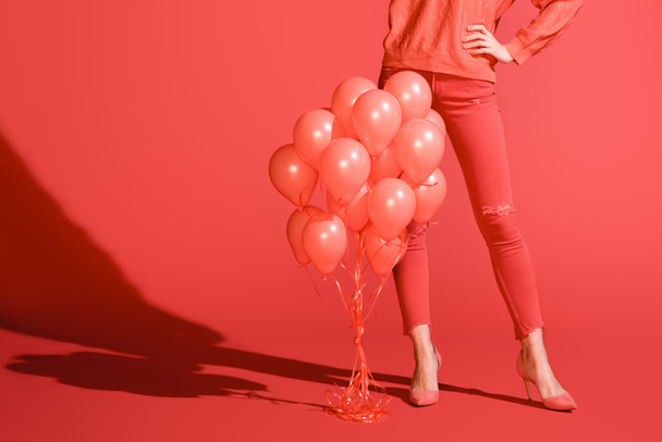 cropped view of fashionable girl posing with living coral balloons. Pantone color of the year 2019 concept - Фото, зображення