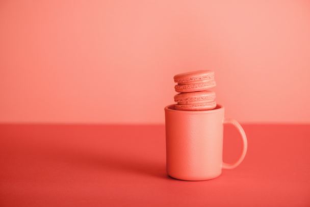 sweet macaroons in cup on Living coral background. Pantone color of the year 2019 concept - Фото, зображення