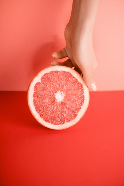 bijgesneden beeld van vrouwelijke hand met grapefruit op levende koraal. PANTONE-kleur van het jaar 2019-concept - Foto, afbeelding