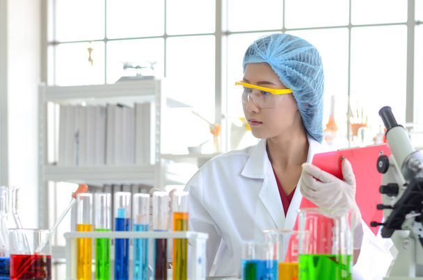 Женщина-ученый в лаборатории проводит эксперименты с химической жидкостью и делает контрольный список и записывает данные из тестирования в лаборатории
. - Фото, изображение