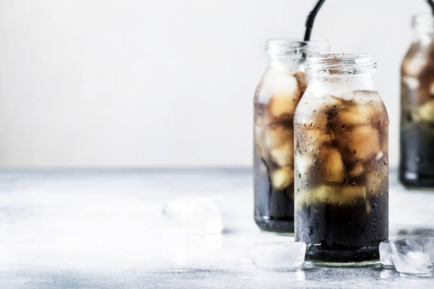 Healthy food and drink concept: cold black detox mineral water with crushed ice in glass bottles, with activated charcoal, gray stone table background, trendy beverage, copy space, selective focus - Foto, imagen