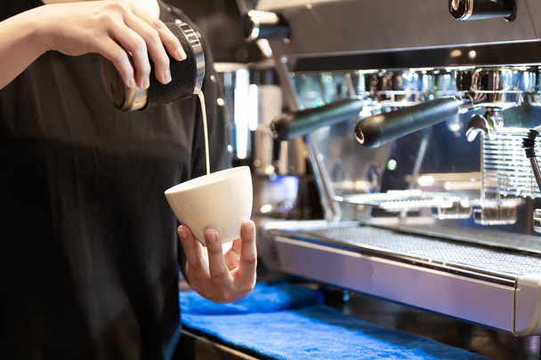Immagine ravvicinata di una barista che versa il latte e prepara cappuccino fresco in piedi davanti alla macchina del caffè al bar al mattino
  - Foto, immagini