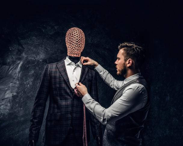 Un diseñador de moda que comprueba la calidad de un elegante traje de hombre hecho a medida en un estudio de sastre oscuro
 - Foto, Imagen