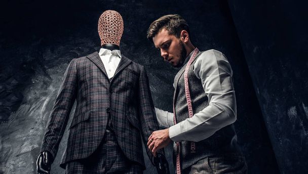 Een mode-ontwerper controle op de kwaliteit van een op maat gemaakt elegant mens past in een donkere kleermaker studio - Foto, afbeelding