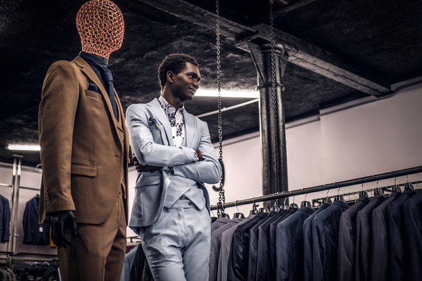 African-American man dressed in blue elegant suit posing with crossed arms in a classic menswear store. - Photo, Image