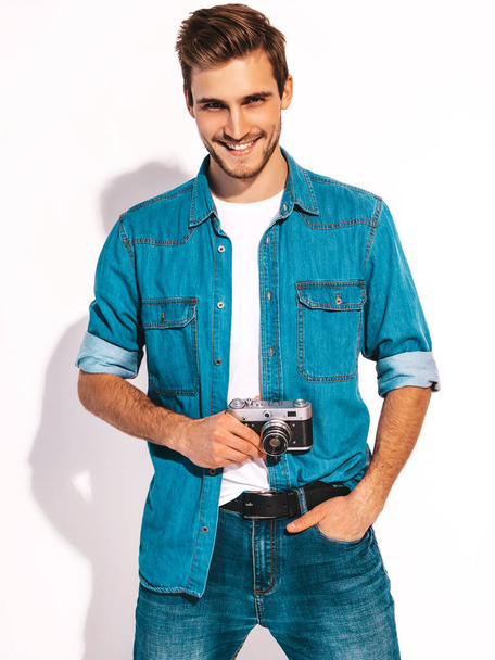 Portrait of handsome smiling man wearing summer hipster jeans clothes. Model male taking picture on old vintage photo camera. Isolated on white - Fotografie, Obrázek