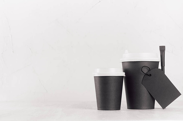 Coffee mockup - different size black paper cups with white caps, blank label and sugar bag on white wood table with copy space, coffee shop interior. Modern elegant concept for branding identity, advertising, design. - Foto, Imagen