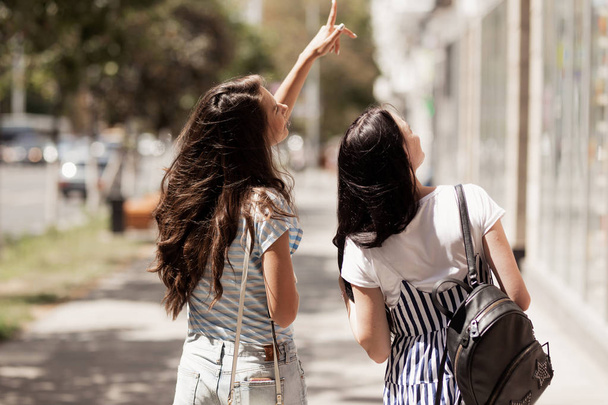 Dos chicas simpáticas y lindas con el pelo largo y oscuro, vestidas con ropa casual, caminan por la calle y se toman de la mano
. - Foto, imagen