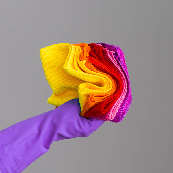 A hand in a rubber glove holds a set of colored microfiber cloths on a neutral background. The concept of bright spring, spring cleaning. - Фото, зображення