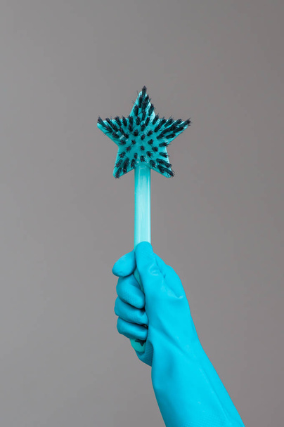 A hand in a rubber glove holds the dishwashing brush on a neutral background. The concept of bright spring, spring cleaning. - Fotografie, Obrázek