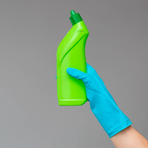A hand in a rubber glove holds a bottle of plumbing detergent on a neutral background. The concept of bright spring, spring cleaning. - Foto, afbeelding