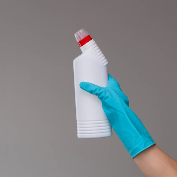 A hand in a rubber glove holds a bottle of plumbing detergent on a neutral background. The concept of bright spring, spring cleaning. - Valokuva, kuva