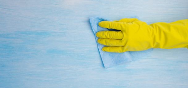 hand in yellow rubber glove, wipes with blue cloth surface, close-up, there is a place for writing - Фото, изображение