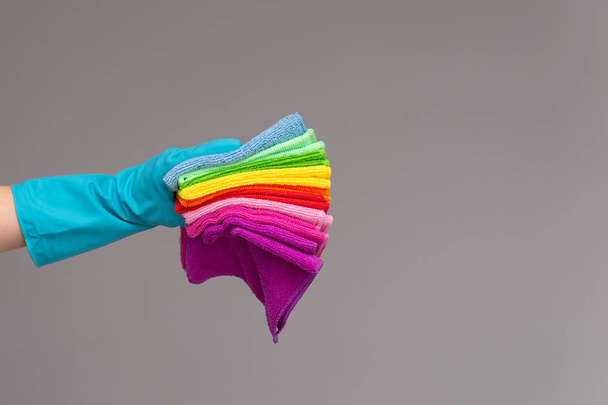 A hand in a rubber glove holds a set of colored microfiber cloths on a neutral background. The concept of bright spring, spring cleaning. - Valokuva, kuva
