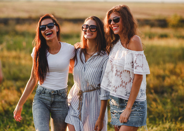Three gorgeous young women in sunglasses stand in the field and smiling on a sunny day. - Foto, Imagem
