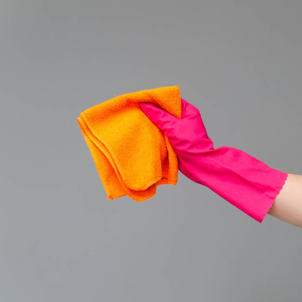 Ruka v gumové rukavici drží světlé mikrovlákno duster na neutrálním pozadí. Jarní úklid koncept. - Fotografie, Obrázek