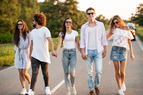 Young happy guys and girls are  holding hands and walking on the road on a sunny day - Foto, imagen